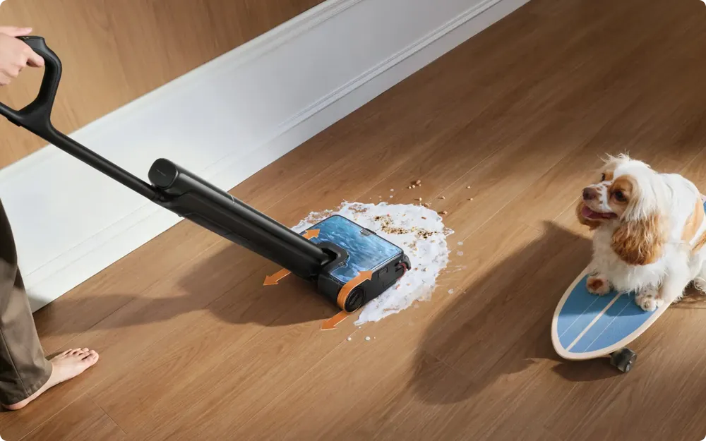 Cordless wet dry vacuum lifting a wet spill and dry crumbs from a wood floor in one pass.