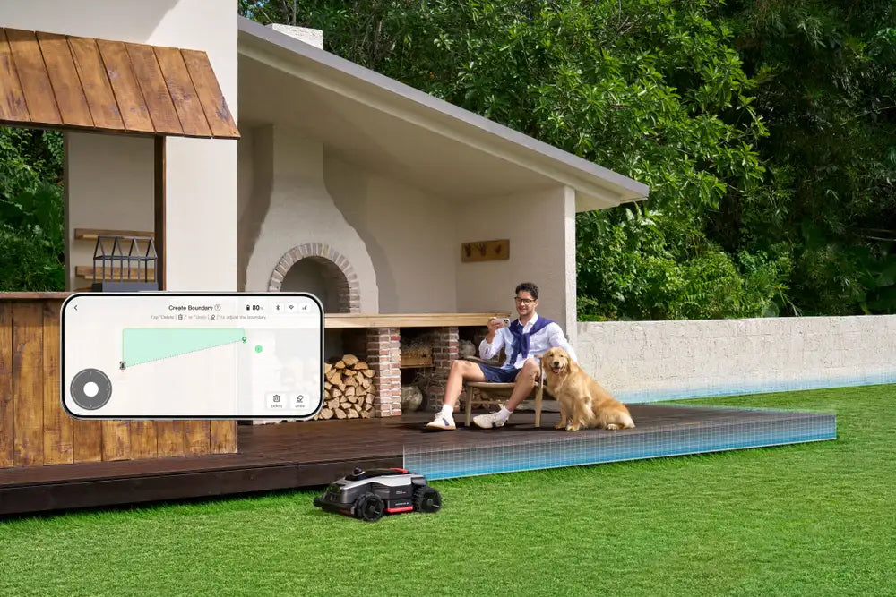 Dreame robot mower on a lawn with a phone screen showing wire-free AI boundary mapping in the app.