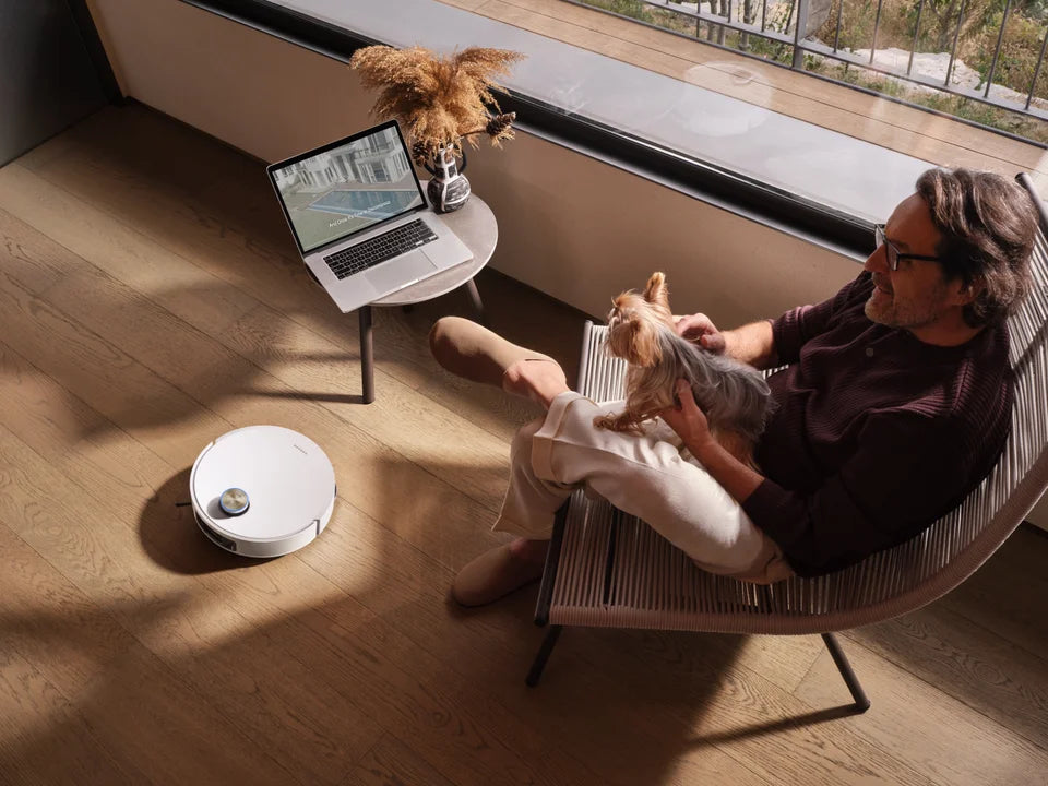 Dreame robot vacuum cleans the floor nearby and a laptop sits on a side table.