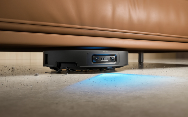 Dreame robot vacuum cleaning dust under a living room sofa on a hardwood floor.